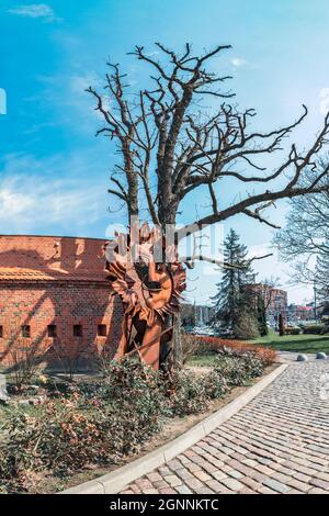 Étrange figure rouillée sous un arbre sans feuilles contre un mur de brique Banque D'Images