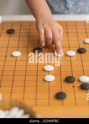 Jeu de Go jeu de jeu de main d'enfant, pierres blanches et noires sur le jeu de plateau, jeu asiatique classique en bois avec lignes de grille, image verticale. Banque D'Images