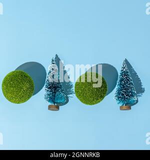 Fond conceptuel de Noël et nouvel an avec petits arbres de noël et boules vertes sur fond bleu. Des ombres dures tendance, prises en studio Banque D'Images