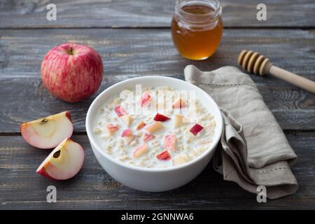 Bouillie de flocons d'avoine au lait avec pomme et miel dans un bol blanc sur une table en bois. Délicieux petit déjeuner maison sain Banque D'Images