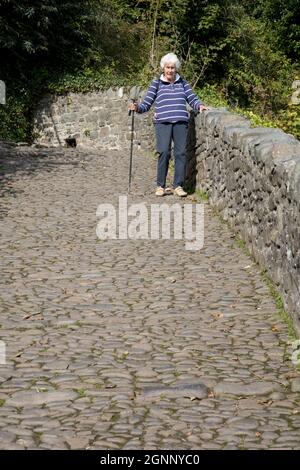 Femme âgée avec hikinh Stick marchant prudemment dans la rue pavée de Clovelly North Devon Banque D'Images