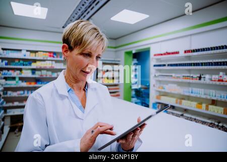 Pharmacien caucasien défilant dans un comprimé numérique debout derrière un comptoir de médicaments en pharmacie Banque D'Images