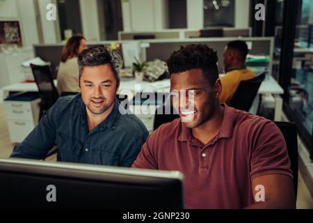 Deux hommes d'affaires de race mixte travaillant sur le projet de collaboration dactylographiant sur un ordinateur de bureau dans un bloc de bureau Banque D'Images