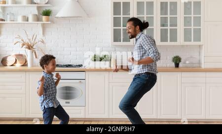 Heureux père afro-américain avec petit fils dansant dans la cuisine Banque D'Images