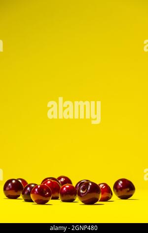 Un bouquet de cerises rouges repose chaotiquement sur un fond jaune vif d'été. Banque D'Images