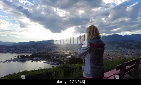 Femme photographe prenant des photos au sommet de la ville de Lugano par le lac de Lugano en Suisse. Belvédère avec vue aérienne depuis la colline de San Michele. Lugano Banque D'Images