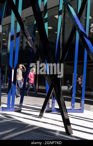 Les ouvriers de la ville marchent devant la sculpture intitulée « Cosmos », une œuvre d'Eva Rothschild dans la ville de Londres, le quartier financier de la capitale, le 24 septembre 2021, à Londres, en Angleterre. COSMOS (2019) est composé de trois structures à lamelles de 3,5 m de haut qui se penchent et se soutiennent mutuellement et fait partie du projet Art in the City de l'été. Banque D'Images