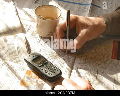 Homme avec une tasse de café et mobile, à la recherche d'un emploi dans un journal, Autriche Banque D'Images