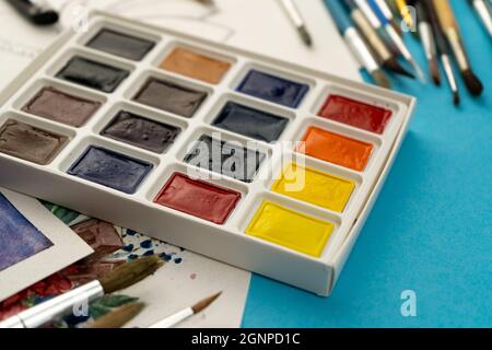Une boîte d'aquarelles avec des pinceaux. Dessin, arrière-plan. Emballage de nouvelles peintures multicolores sur la table. Brossez et peignez. Dessin et hobbie. Banque D'Images