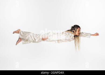 femme afro-américaine en pyjama de soie lévitant dans le sommeil isolé sur blanc Banque D'Images