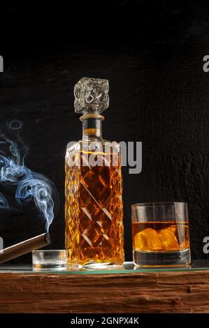 Élégante bouteille de whisky avec verre et glace et cigare sur une table en bois Banque D'Images