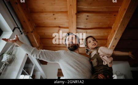 Vue à angle bas de père mûr avec petite fille debout à l'intérieur à la maison, tenant et tenant. Banque D'Images