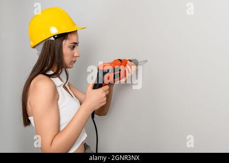 Une jeune femme travaille à percer un trou sur le mur pour la construction ou la rénovation. Photo de haute qualité Banque D'Images