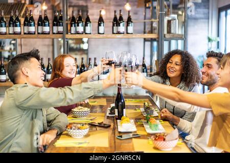 Des amis multiculturels dégustent du vin rouge au restaurant du bar à sushis - concept de mode de vie gastronomique avec des jeunes qui s'amusent ensemble à manger un poke Bowl - Brig Banque D'Images