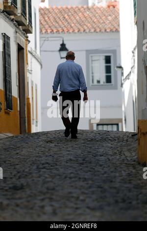 Rue en pierre par des maisons blanches et jaunes typiques. Homme marchant seul. Evora. Portugal. Banque D'Images