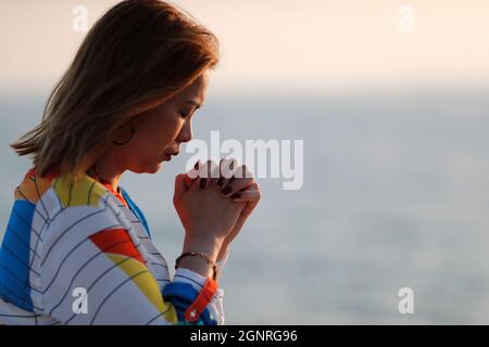 Femme fidèle priant, mains pliées dans l'adoration à dieu, tête vers le bas, yeux fermés dans la ferveur religieuse. Banque D'Images