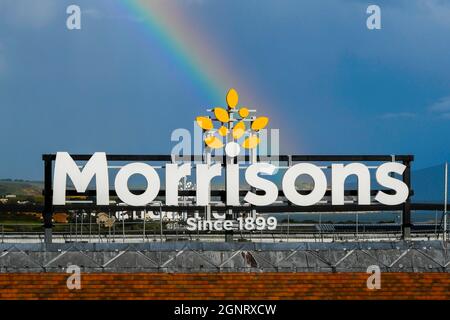 Weymouth, Dorset, Royaume-Uni. 27 septembre 2021. Météo Royaume-Uni. Un arc-en-ciel s'épare dans le ciel au-dessus d'un panneau de supermarché Morrisons à Weymouth à Dorset, le soleil se couche après une douche à forte pluie. Crédit photo : Graham Hunt/Alamy Live News Banque D'Images