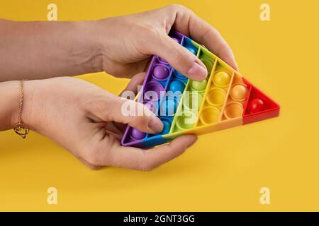 Hans femelle utilisant l'antistress jouet popit arc-en-ciel pour les enfants et les adultes sur fond jaune. Jouet anti-stress sensoriel flexible, forme ronde, cop Banque D'Images