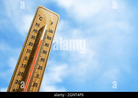 Thermomètre en bois avec liquide de mesure rouge indiquant une température élevée de plus de 32 degrés Celsius sur fond de ciel bleu avec nuages. Concept de chaleur W Banque D'Images