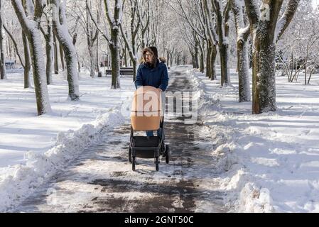 Le père marche avec une poussette dans un parc couvert de neige en hiver. Passer du temps avec un bébé dans une belle journée d'hiver. Promenades récréatives avec un enfant. M Banque D'Images