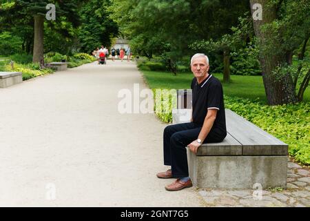 Vue en longueur d'un homme senior assis sur un banc de parc regardant la caméra Banque D'Images