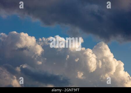 Lourds nuages sombres sur fond bleu ciel, rayons de soleil à travers les nuages. Nuages cumulus moelleux, couleur blanc et gris Banque D'Images