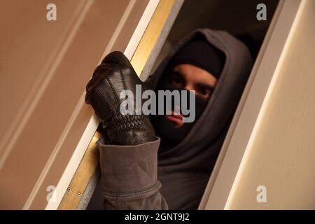 Le concept de maison, de cambriolage. Cambrioleur masqué en balaclava noir ouvrant la porte, entrant illégalement dans la maison Banque D'Images