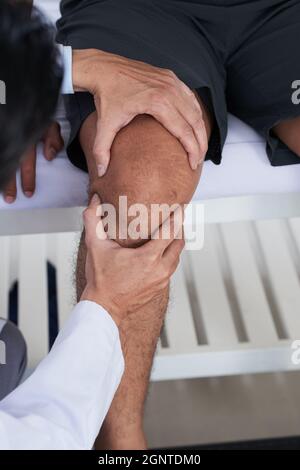 Gros plan vertical moyen d'un physiothérapeute professionnel réalisant la palpation du genou des patients Banque D'Images