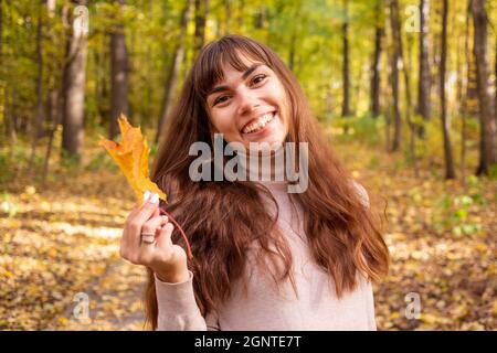 jeune belle femme avec feuille d'automne souriant à la caméra dans le parc d'automne au soleil brille Banque D'Images