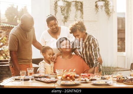 Portrait d'une heureuse grand-mère afro-américaine célébrant son anniversaire en famille lors d'un dîner à l'extérieur, éclairée par la lumière du soleil Banque D'Images