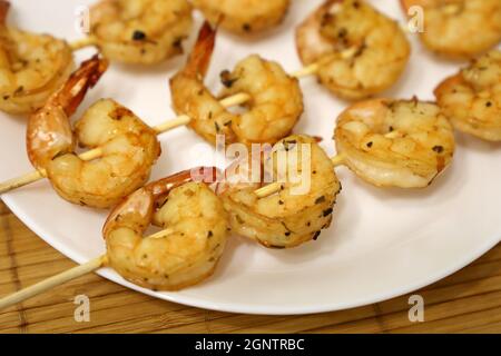 Crevettes royales grillées aux épices. Brochettes de bois aux crevettes sur une assiette blanche, délicieux plat Banque D'Images
