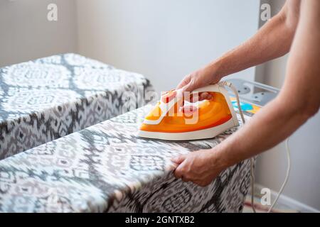 Un homme avec un fer à repasser dans ses mains, repassant du linge sur une planche à repasser. Travaux ménagers et nettoyage. Répartition des tâches. Banque D'Images