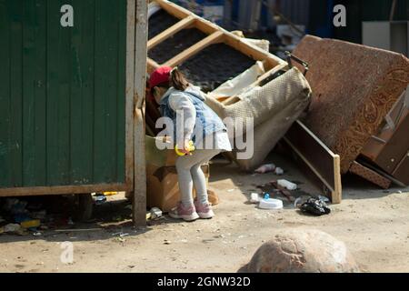 Un enfant dans un jardin. La fille goutte à goutte dans la poubelle. L'enfant a trouvé le jouet dans le tas de déchets. La pauvre fille marche seule. Banque D'Images