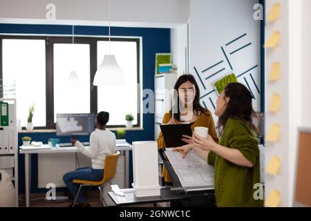 Équipe de femmes d'affaires debout dans le bureau de studio créatif discutant et analysant le prototype de mesure de modèle de bâtiment avec un crayon. Collègues de planification de conception d'idées de construction dans le milieu de travail multimédia Banque D'Images