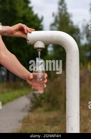 Gros plan de la bouteille en verre de remplissage pour les mains d'une femme avec de l'eau provenant d'un robinet public gratuit Banque D'Images