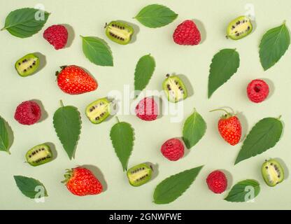 Fruit d'actinidia arguta, fruits aux baies de kiwi, framboises, fraises et feuilles de menthe, sur fond vert. Banque D'Images
