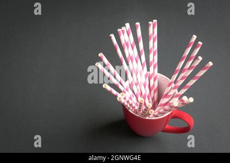 Paillettes de papier à rayures roses à l'intérieur d'une tasse rouge, sur fond noir. Copier l'espace. Banque D'Images