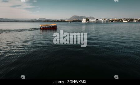 Un bateau de couleur orange sur le lac bleu Pichola pendant la lumière du jour à Udaipur, Rajasthan Banque D'Images