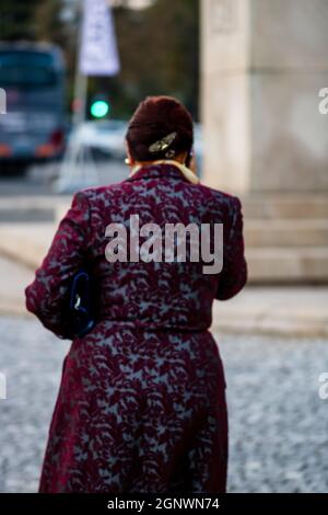 Vue arrière d'une femme âgée élégante qui marche dans la rue tout en parlant au téléphone Banque D'Images