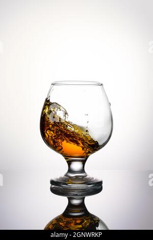 Une éclaboussure de cognac dans un verre isolé sur un arrière-plan léger. Banque D'Images