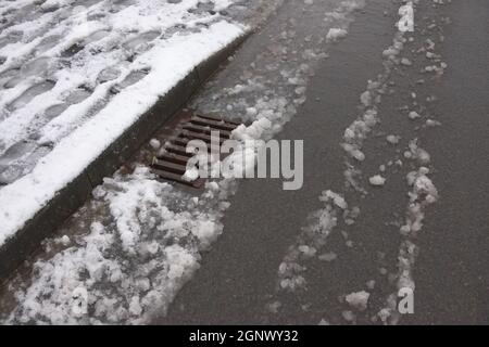 5 - route urbaine et trottoir couverts de neige épaisse qui commence à dégeler. Le drain de tempête au niveau de la surface traite de l'eau qui en résulte. Banque D'Images