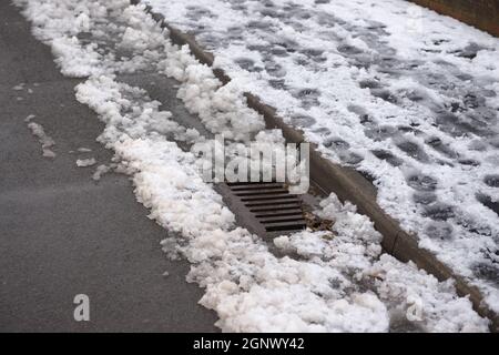 12 - scène urbaine de pas dans un pavé plein de neige. Le drain ressort de l'accumulation de neige sur le côté de la route. Scène environnementale d'hiver Banque D'Images