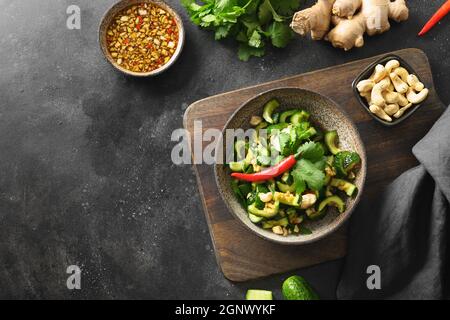 Salade asiatique épicée de concombres brisés avec coriandre, gingembre, piment, vinaigre noir sur fond noir avec espace de copie. Concombres épicés. Vue de Banque D'Images