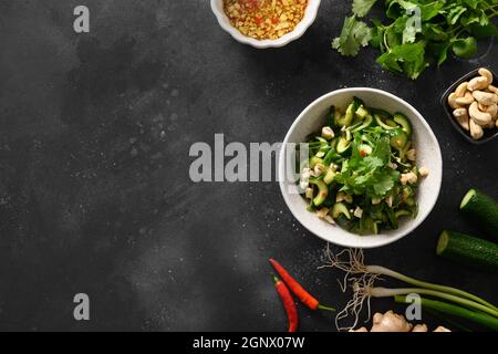Salade asiatique épicée de concombres brisés avec coriandre, gingembre, piment, vinaigre noir sur fond noir avec espace de copie. Concombres épicés. Vue de Banque D'Images
