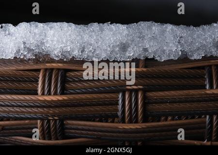 Une couche de glace se couche sur le dessus du mobilier de jardin en plastique texturé. Copier l'espace sur fond noir, composition plein cadre. Apparence de la corde comme une macro Banque D'Images