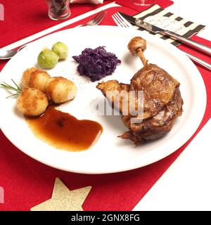 Cuisse de canard rôtie avec bacon choux de Bruxelles et chou rouge et boulettes sur une assiette blanche, menu des fêtes, dîner de Noël. Banque D'Images