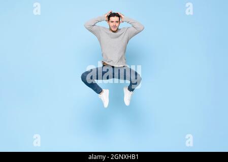 Jeune homme beau se sentant submergé de sauter avec les mains sur la tête dans la couleur bleu clair isolé de fond de studio Banque D'Images