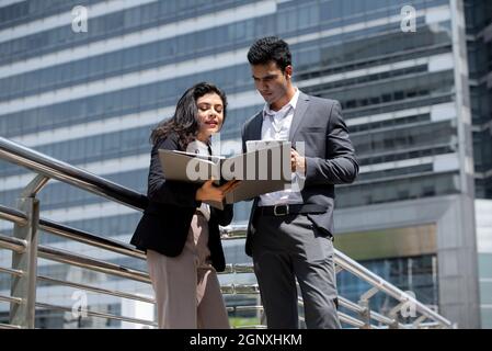 Beau jeune homme d'affaires indien en tenue d'entreprise discutant avec une femme d'affaires à l'extérieur dans la ville Banque D'Images