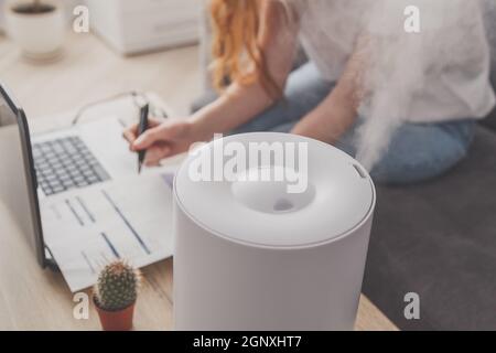 Femme freelance utilise un humidificateur domestique sur le lieu de travail pour maintenir l'humidité relative et le microclimat sur le lieu de travail du bureau à domicile avec Banque D'Images