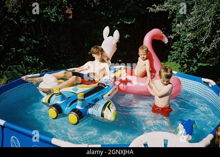 Trois garçons jouant dans une piscine de jardin, Medstead, Hampshire, Angleterre, Royaume-Uni. Banque D'Images